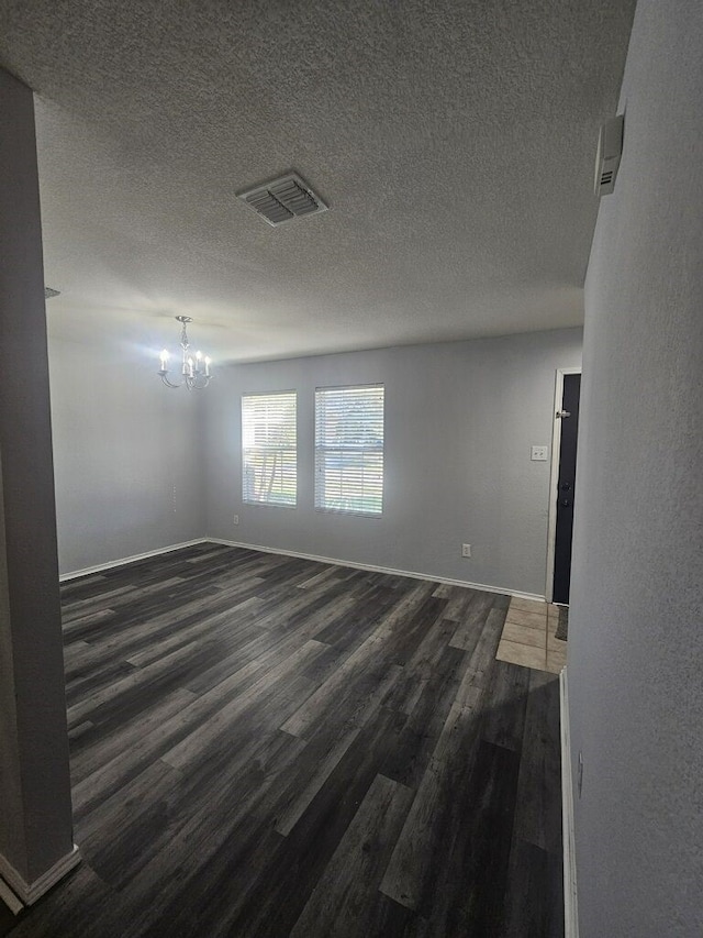 empty room with a textured ceiling, dark hardwood / wood-style floors, and a notable chandelier