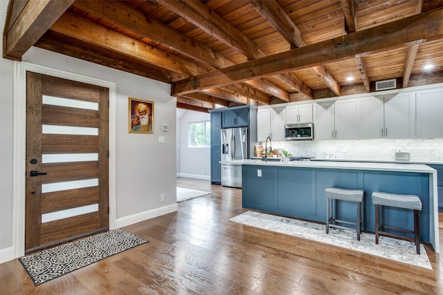 kitchen featuring white cabinets, appliances with stainless steel finishes, wooden ceiling, light wood-type flooring, and beamed ceiling