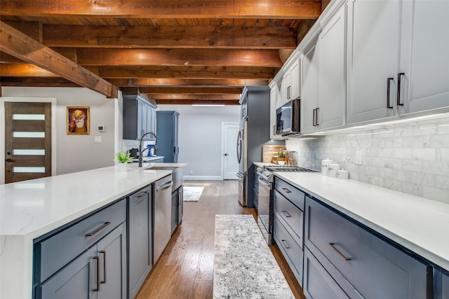 kitchen featuring sink, light wood-type flooring, backsplash, stainless steel appliances, and beam ceiling