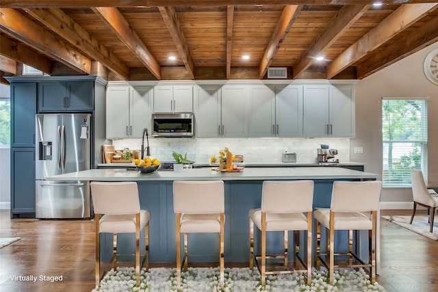 kitchen with appliances with stainless steel finishes, a kitchen island with sink, dark wood-type flooring, and a kitchen bar