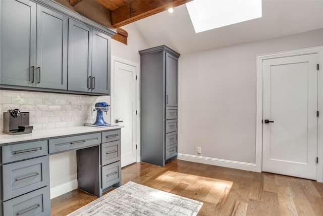 kitchen with light hardwood / wood-style floors, lofted ceiling with skylight, tasteful backsplash, and gray cabinetry