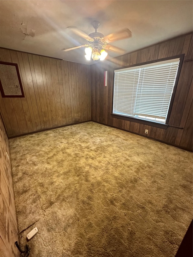 carpeted spare room with wood walls and ceiling fan