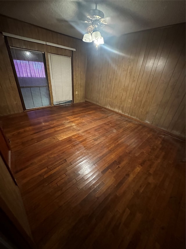 unfurnished bedroom featuring wood-type flooring, a textured ceiling, wooden walls, and ceiling fan