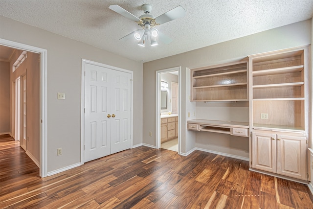 unfurnished office with ceiling fan, dark hardwood / wood-style flooring, built in desk, and a textured ceiling