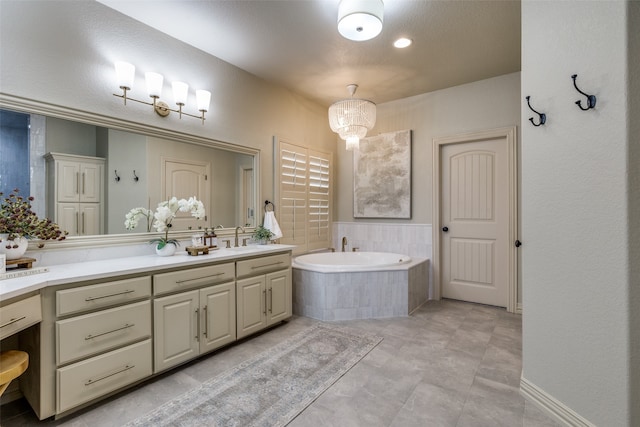 bathroom with an inviting chandelier, tile patterned flooring, tiled bath, and vanity