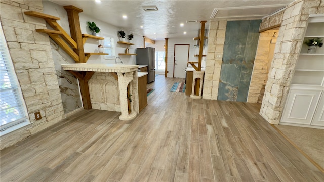 bar with stainless steel refrigerator, light hardwood / wood-style flooring, and a healthy amount of sunlight