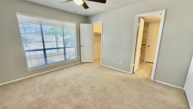 unfurnished bedroom featuring light carpet, a spacious closet, and ceiling fan