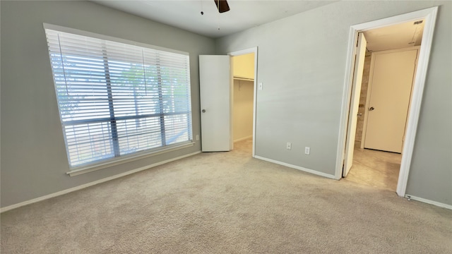 unfurnished bedroom with light colored carpet, ceiling fan, a walk in closet, and a closet