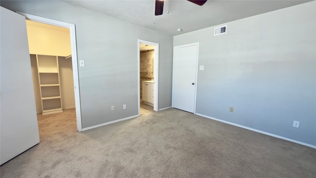 unfurnished bedroom featuring light carpet, a closet, ceiling fan, and a walk in closet