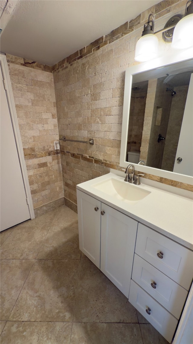 bathroom featuring walk in shower, vanity, and brick wall