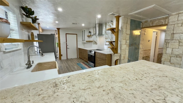 kitchen featuring stainless steel electric stove, wall chimney exhaust hood, kitchen peninsula, sink, and black fridge