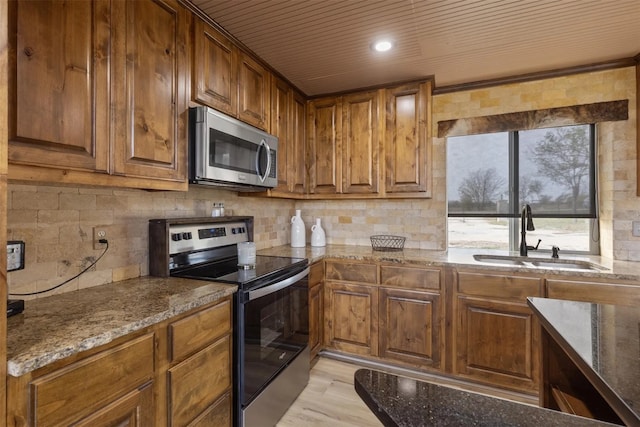 kitchen featuring appliances with stainless steel finishes, backsplash, stone countertops, light hardwood / wood-style flooring, and sink