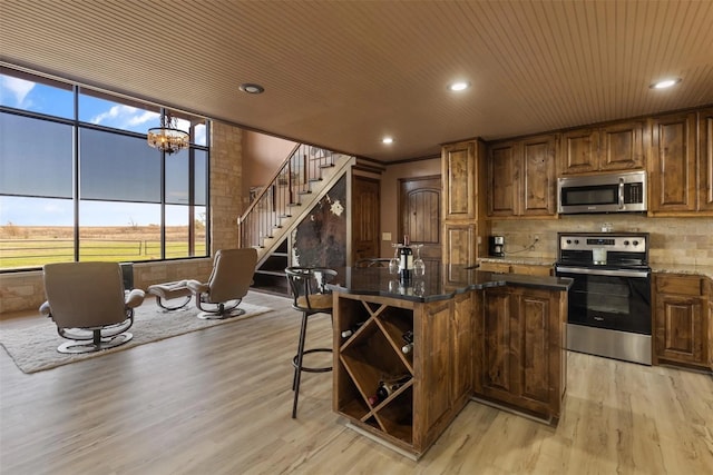 kitchen featuring appliances with stainless steel finishes, decorative backsplash, an island with sink, wooden ceiling, and light hardwood / wood-style flooring