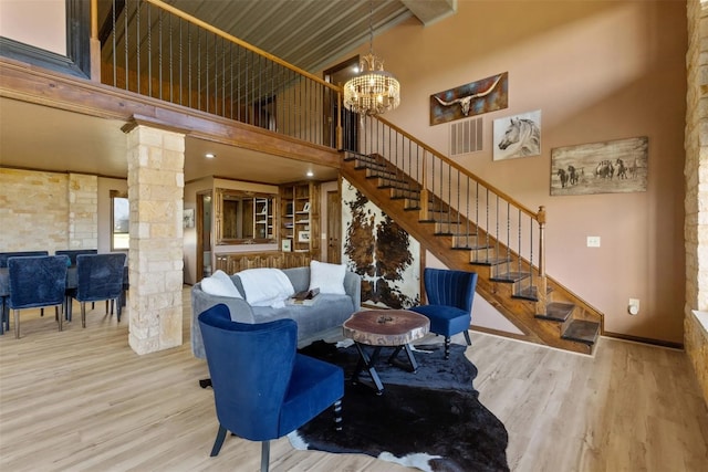 living room featuring an inviting chandelier, hardwood / wood-style flooring, a towering ceiling, and ornate columns