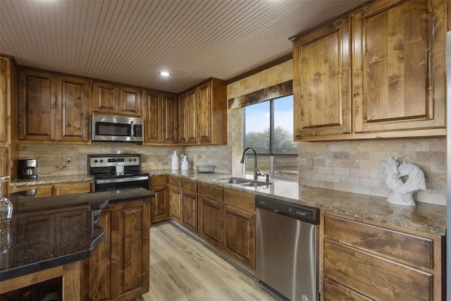 kitchen featuring appliances with stainless steel finishes, light hardwood / wood-style floors, dark stone countertops, backsplash, and sink