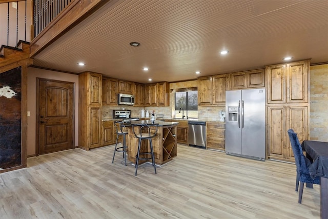 kitchen featuring appliances with stainless steel finishes, light wood-type flooring, a kitchen island, and a breakfast bar