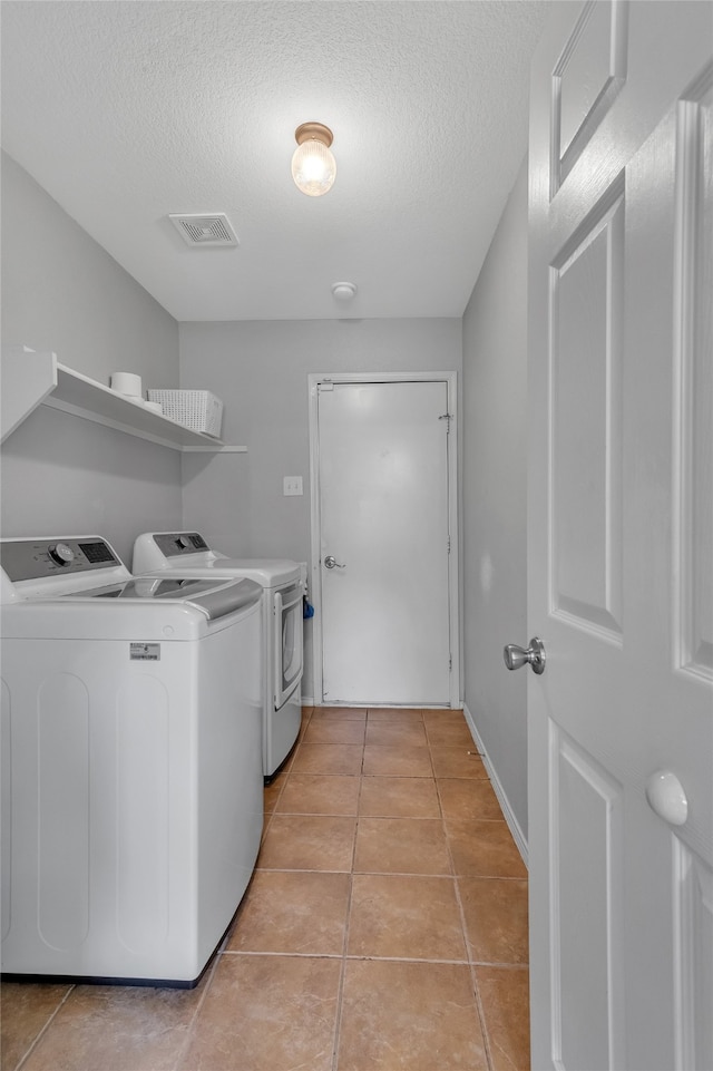 washroom featuring washing machine and clothes dryer, a textured ceiling, and light tile patterned floors