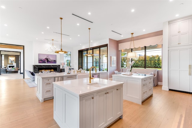 kitchen with white cabinetry, sink, light hardwood / wood-style flooring, an island with sink, and pendant lighting