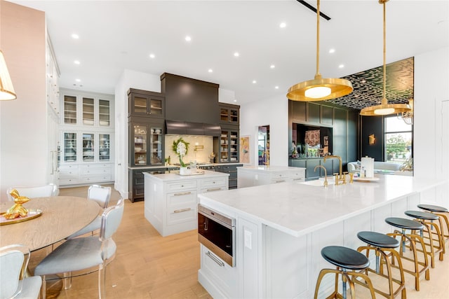 kitchen with light wood-type flooring, a large island with sink, decorative light fixtures, white cabinets, and stainless steel microwave