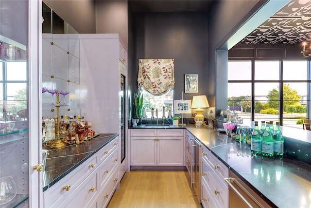 kitchen with light wood-type flooring, white cabinetry, dark stone counters, and sink