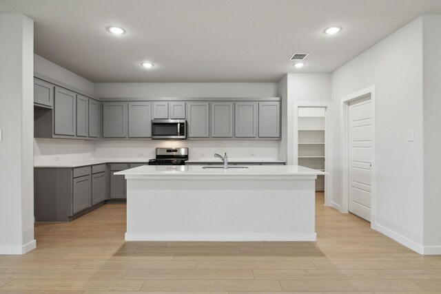kitchen featuring appliances with stainless steel finishes, light wood-type flooring, a sink, gray cabinetry, and visible vents