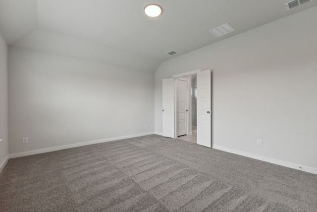 carpeted empty room with baseboards, visible vents, and vaulted ceiling