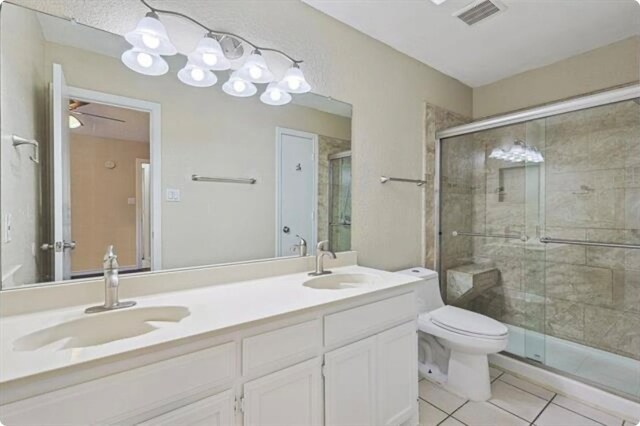 bathroom with tile patterned flooring, a shower with door, ceiling fan, vanity, and toilet