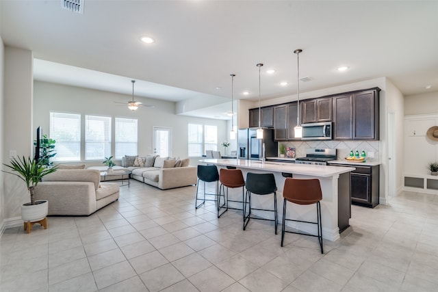 kitchen with dark brown cabinetry, stainless steel appliances, tasteful backsplash, a breakfast bar area, and a kitchen island with sink