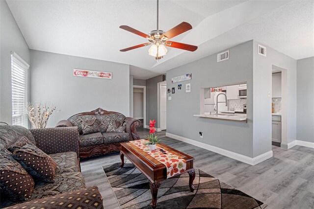 living room featuring ceiling fan, lofted ceiling, hardwood / wood-style floors, and a textured ceiling