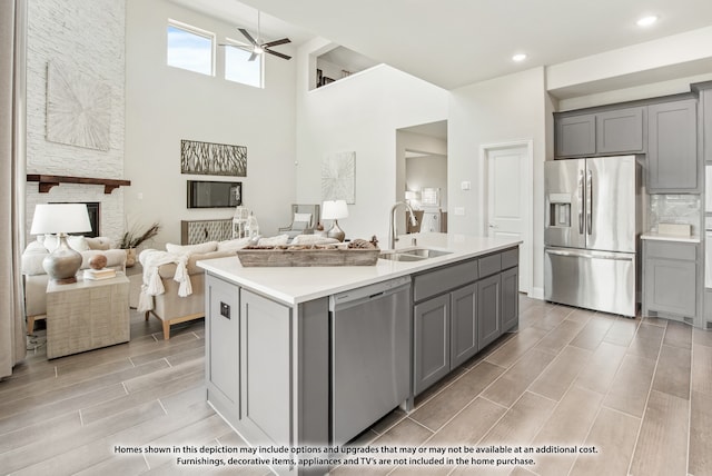 kitchen featuring sink, a kitchen island with sink, gray cabinets, appliances with stainless steel finishes, and a towering ceiling