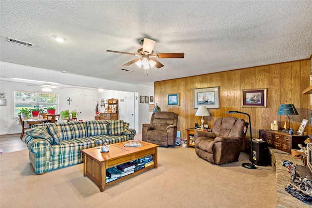 carpeted living room featuring ceiling fan, a textured ceiling, and wooden walls