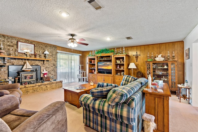 carpeted living room with ceiling fan, a textured ceiling, wooden walls, and a wood stove