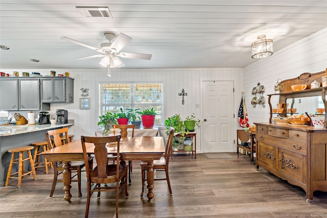 dining space with ceiling fan, wooden walls, and dark wood-type flooring