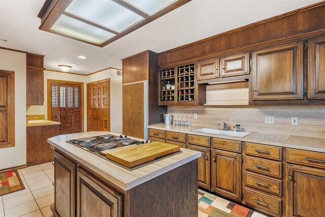 kitchen with light tile patterned floors, sink, tasteful backsplash, stainless steel gas stovetop, and a center island