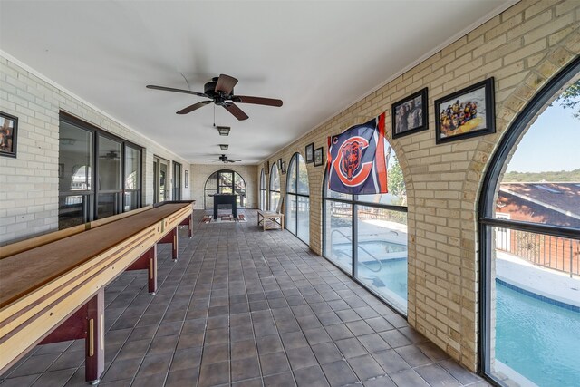 rec room with ornamental molding, ceiling fan, and brick wall