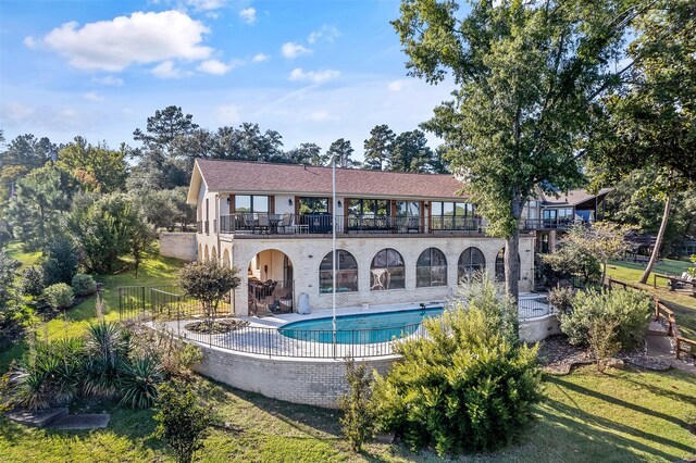 back of house with a balcony, a patio, a fenced in pool, and a lawn