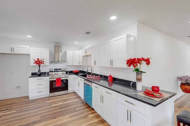 kitchen featuring appliances with stainless steel finishes, wall chimney range hood, light hardwood / wood-style floors, and white cabinets