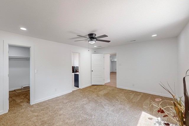 unfurnished bedroom featuring a walk in closet, a closet, carpet flooring, and ceiling fan