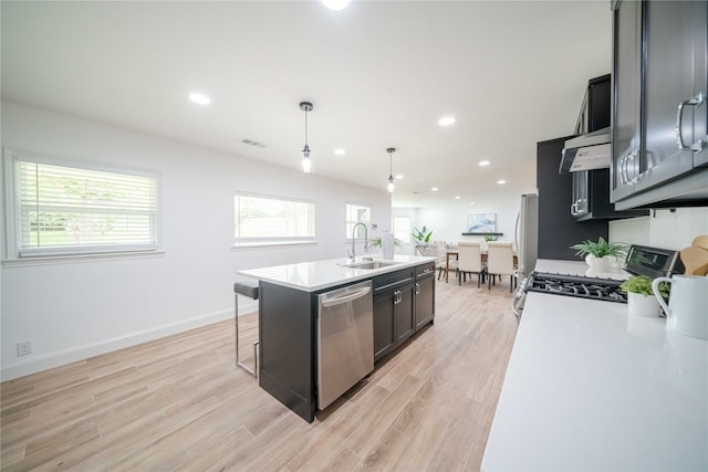 kitchen with appliances with stainless steel finishes, light wood-type flooring, decorative light fixtures, a center island with sink, and sink