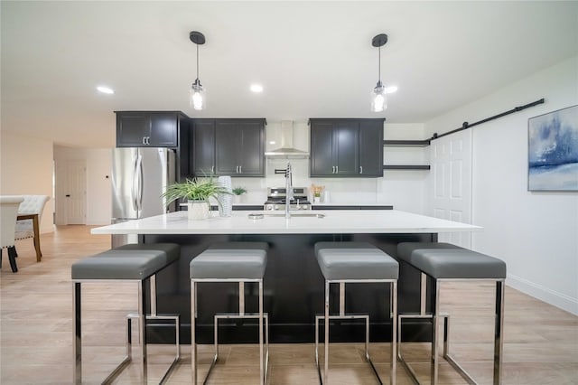 kitchen with pendant lighting, stainless steel appliances, wall chimney range hood, and a barn door