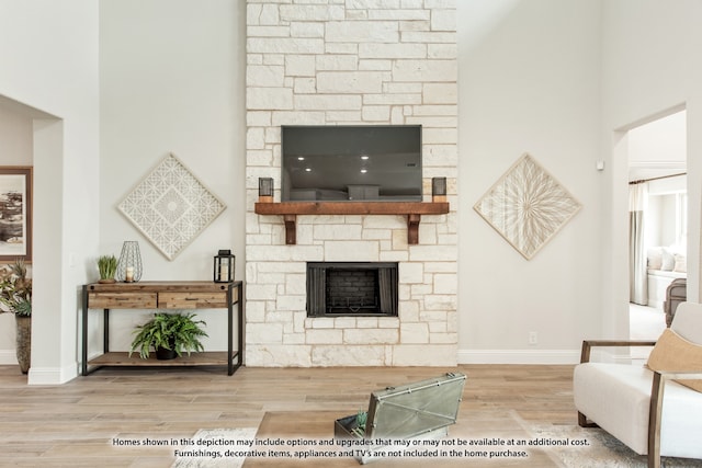 living room featuring wood-type flooring, a towering ceiling, and a stone fireplace