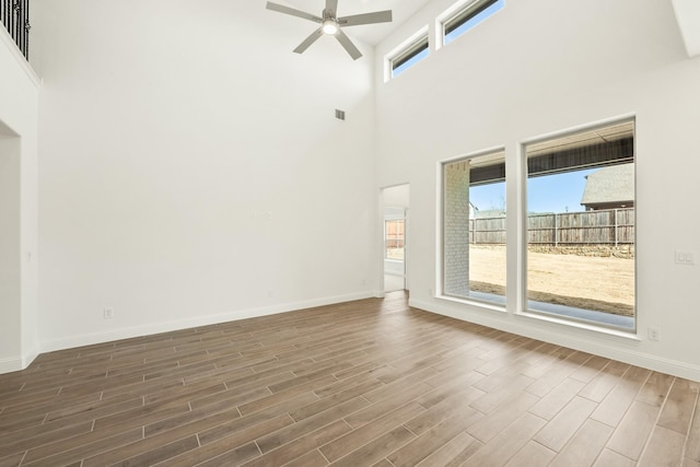 spare room featuring ceiling fan, a high ceiling, visible vents, baseboards, and wood tiled floor