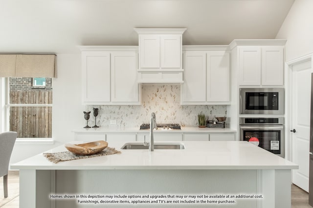 kitchen featuring an island with sink, sink, white cabinetry, stainless steel appliances, and light hardwood / wood-style floors