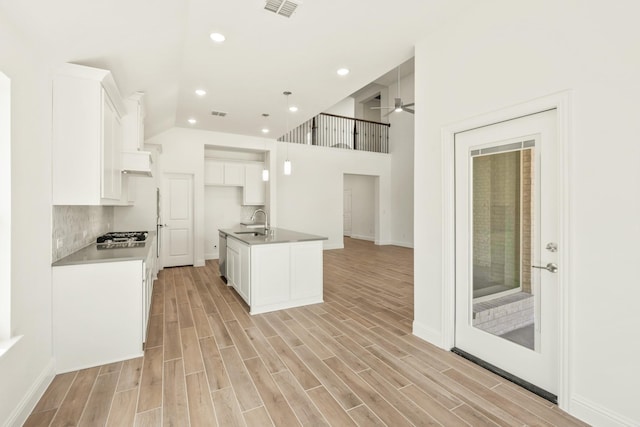 kitchen with a center island with sink, visible vents, wood finish floors, white cabinetry, and pendant lighting