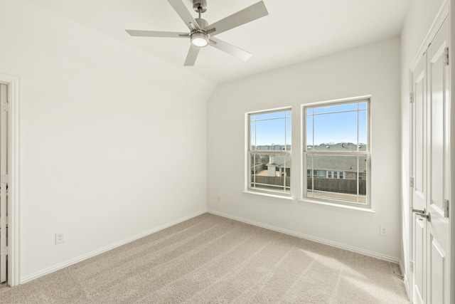 empty room with a ceiling fan, lofted ceiling, light colored carpet, and baseboards