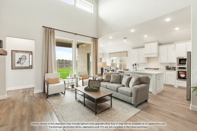 living room featuring light hardwood / wood-style flooring, plenty of natural light, sink, and high vaulted ceiling