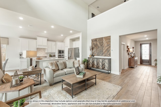 living room featuring light hardwood / wood-style flooring, high vaulted ceiling, and sink