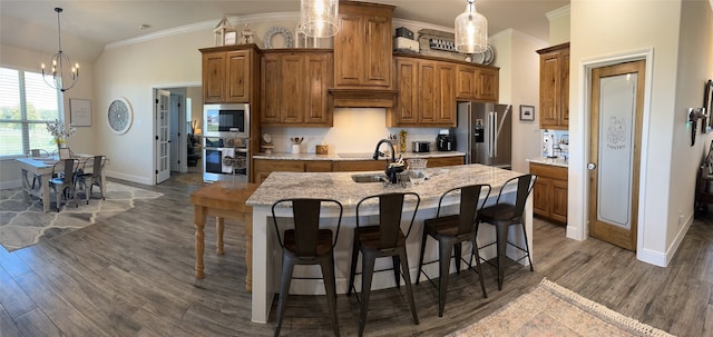 kitchen with dark wood-type flooring, an island with sink, appliances with stainless steel finishes, decorative light fixtures, and a chandelier