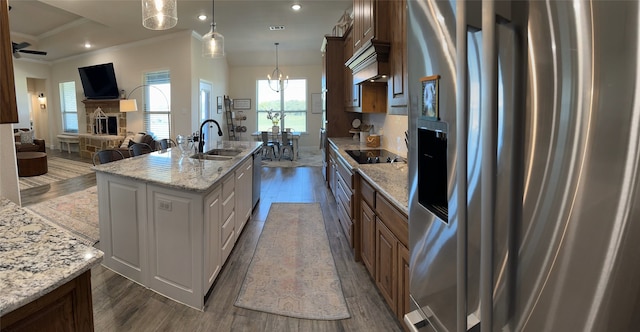 kitchen featuring a center island with sink, crown molding, light stone countertops, appliances with stainless steel finishes, and decorative light fixtures