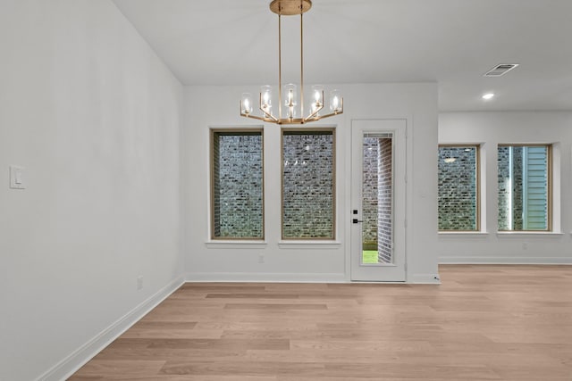 unfurnished dining area with an inviting chandelier and light wood-type flooring